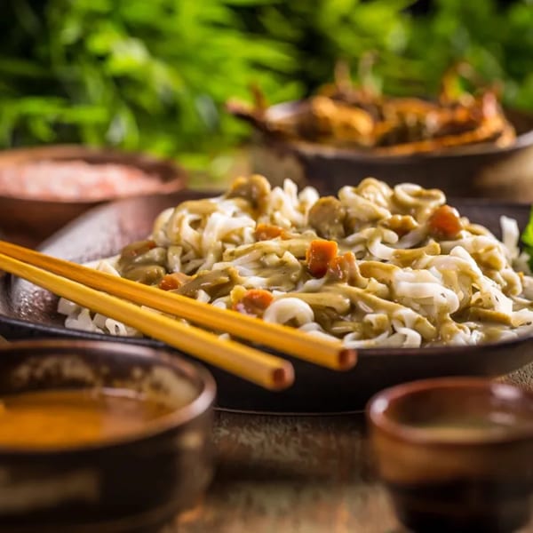 Asian noodles with sauce and vegetables, served with chopsticks and small bowls.
