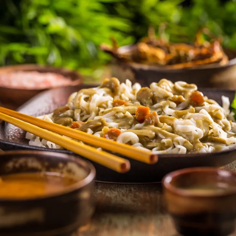 Asian noodles with sauce and vegetables, served with chopsticks and small bowls.