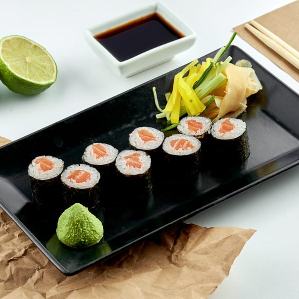 Kami Sushi salmon maki rolls with wasabi, ginger, cucumber, and soy sauce on a black plate.