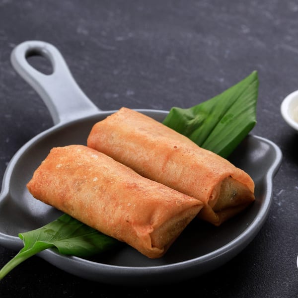 Two golden-brown spring rolls with green leaves on a dark gray serving dish.