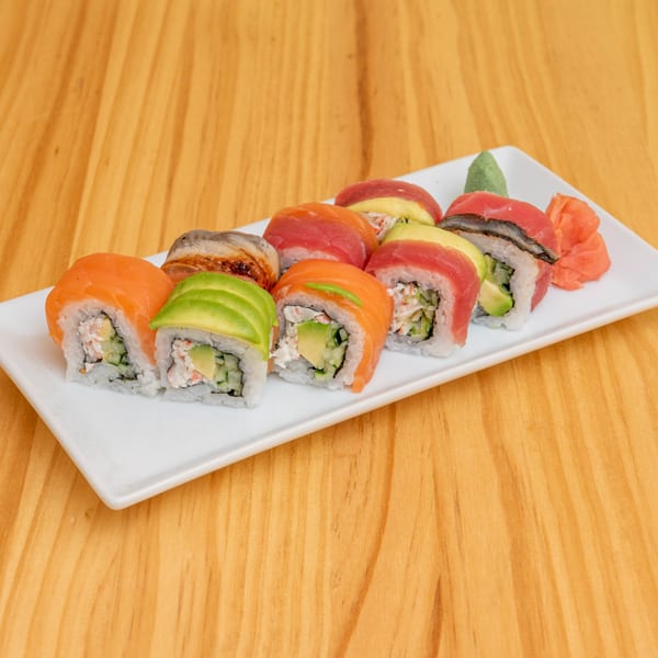 A white rectangular plate holds various sushi rolls, including salmon, tuna, and avocado, on a wooden table.