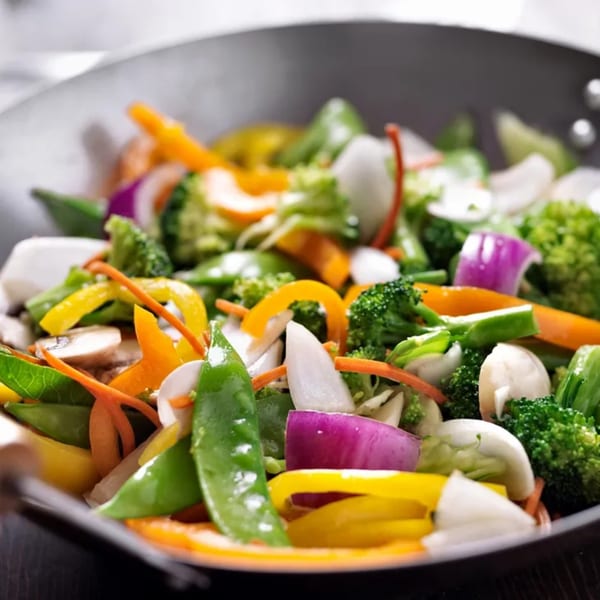 Colorful stir-fried vegetables, including broccoli, carrots, bell peppers, and onions, in a wok.